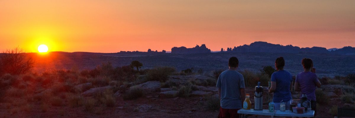 A family enjoys the sun rising above Arches National Park durning Desert Sunrise Mountain Bike Tour