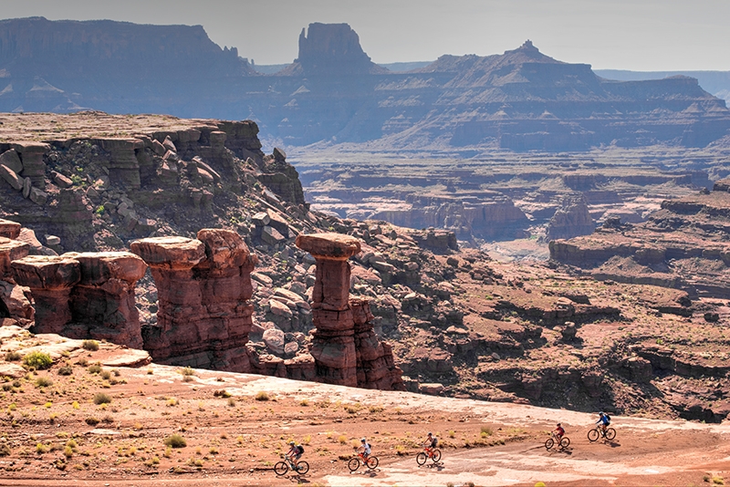The White Rim Trail, located in the Island-In-The-Sky District of Canyonlands National Park, is a true back country escape into desert wilderness. It features breathtaking views, massive red cliffs, sweeping arches, ancient Indian granaries and endless exploring opportunities. There are many ways to experience The White Rim. The easiest way is to view it from any of the pavement-accessible mesa-top overlooks in Island-In-The-Sky, but to really experience The White Rim you need get up close and personal. To do that on your own you’ll need to get either a day use or overnight permit from the park service. However, The White Rim is extremely popular, so permits tend to sell out quickly. Another, much easier, way to experience The White Rim is via a guided mountain bike tour and there are several kinds to choose from. White Rim In A Day specialty tours are offered by different outfitters, but let’s be honest — doing The White Rim in a single day is only for a very select (insane) group of people who are into a massively long day over rough terrain that finishes with a huge climb (often in the dark.) Most people want to spend enough time on their tour so that they can drink in the amazing views and relish the other worldly landscape, so typically, White Rim tours are 3 or 4 days in length.